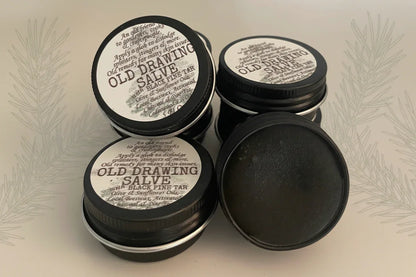 Multiple small metal tins with black lids, each labeled 'OLD DRAWING SALVE with Black Pine Tar'.