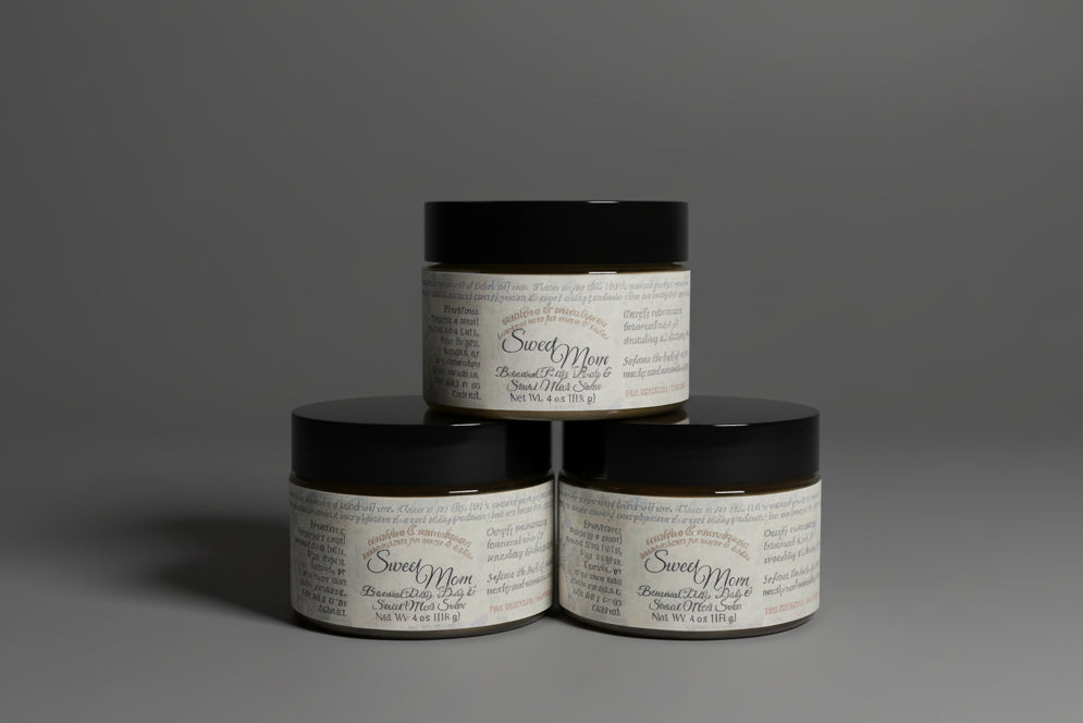 three jars of Sweet Mom Stretch Mark Cream  with labels on a dark surface